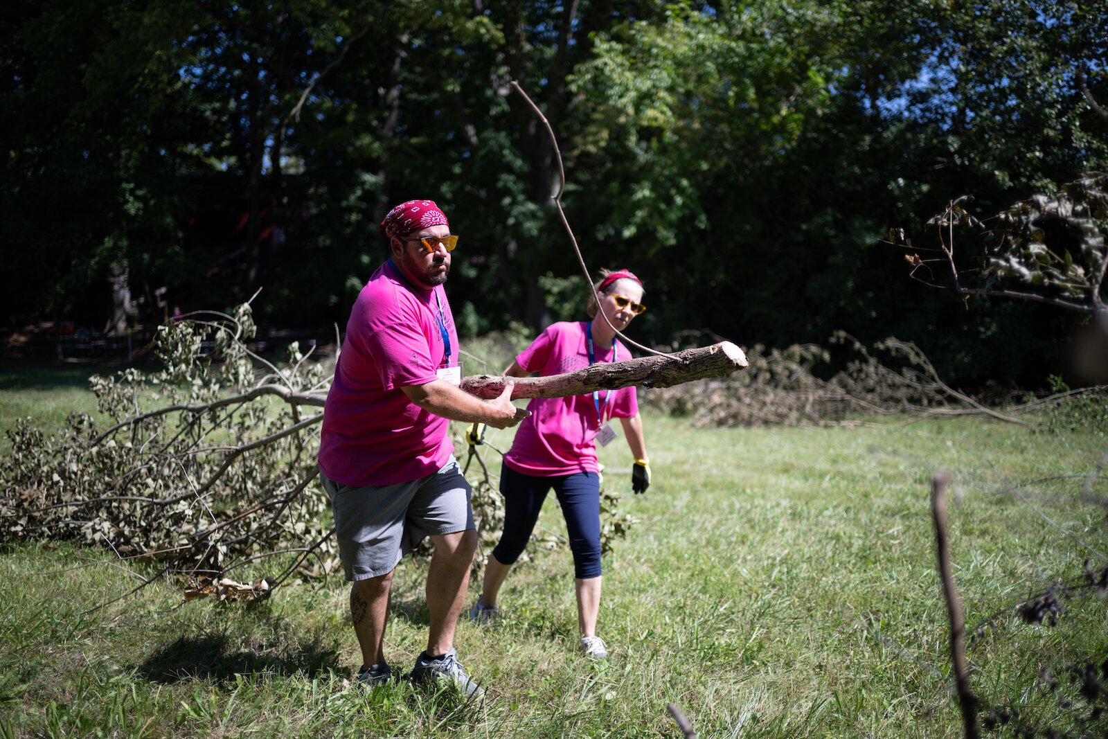 Amazing Race participants pick up tree limbs.