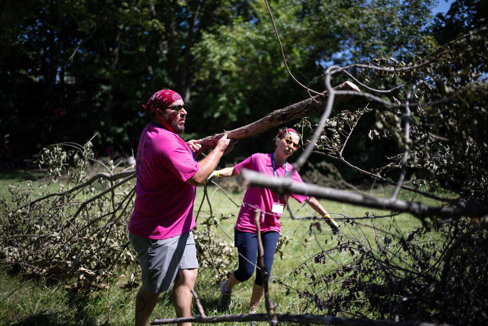 Amazing Race participants pick up tree limbs.
