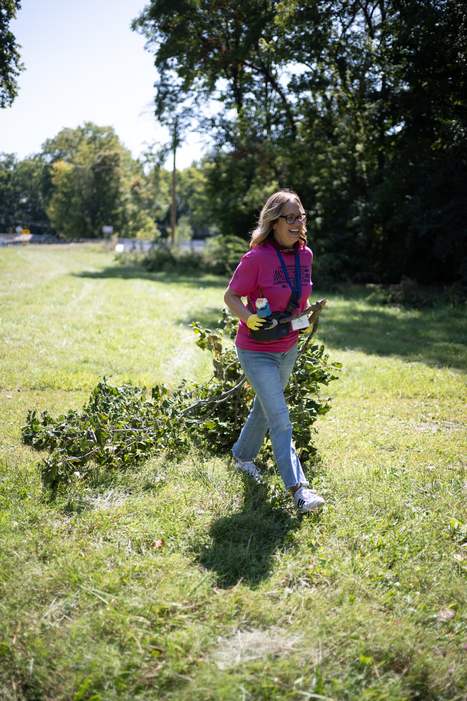 Amazing Race participants pick up tree limbs.