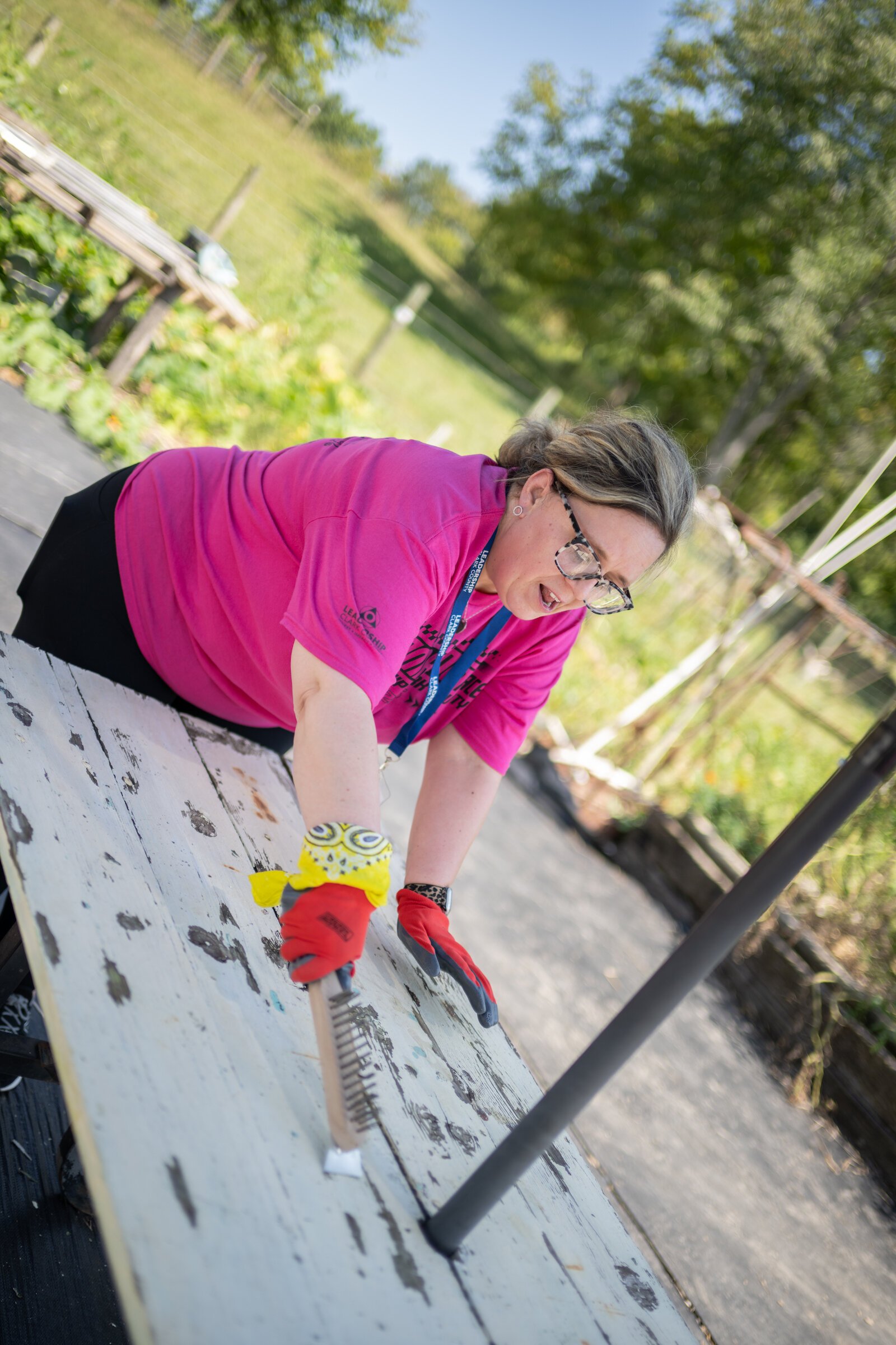 Amazing Race participants strip picnic tables of old paint and apply a new coat of paint.