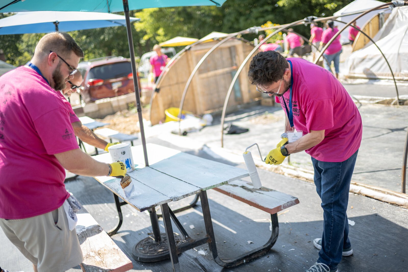 Working together, Amazing Race participants strip picnic tables of old paint and apply a new coat of paint.