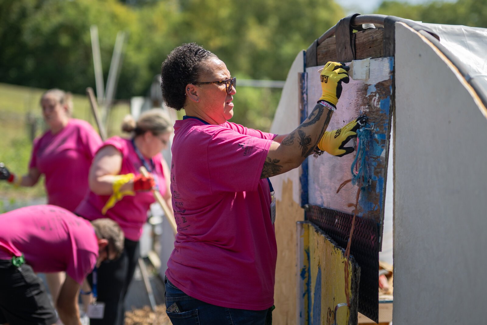 An Amazing Race participant paints the exterior of a greenhouse.