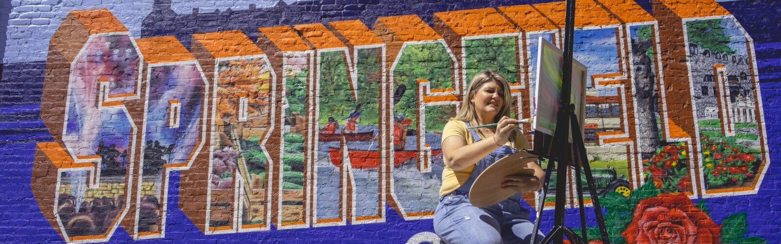 Tracey Tackett works on a painting in front of the Welcome to Springfield mural next to her shop, Sip and Dipity Paint Bar.